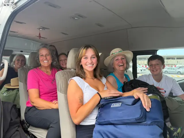 Six guests of three generations seated inside the van on the way to the beach