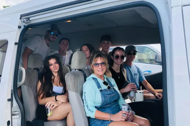Eight friends in their twenties filling a private transfer van, doors open at the pier