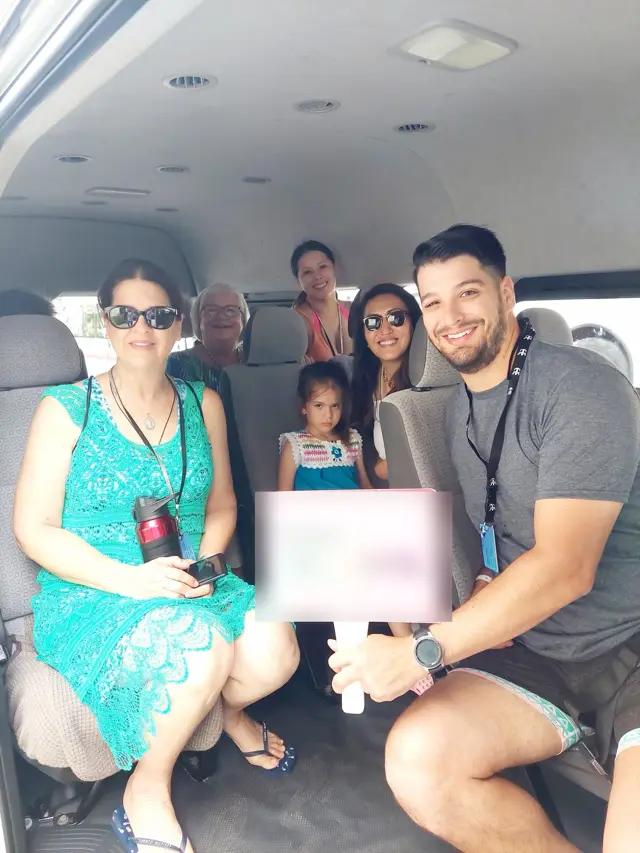 A full van of guests with their driver, three generations aboard, on the way to the beach